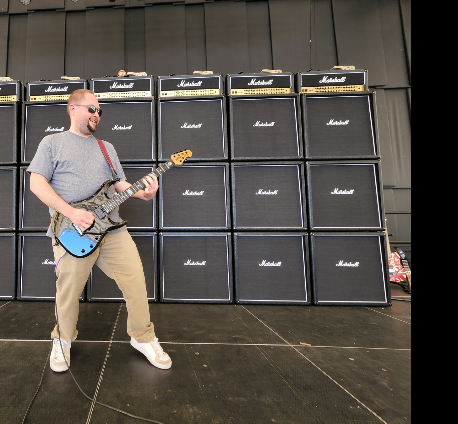 Alex Fernandez playing guitar in front of a Marshall amplifier wall